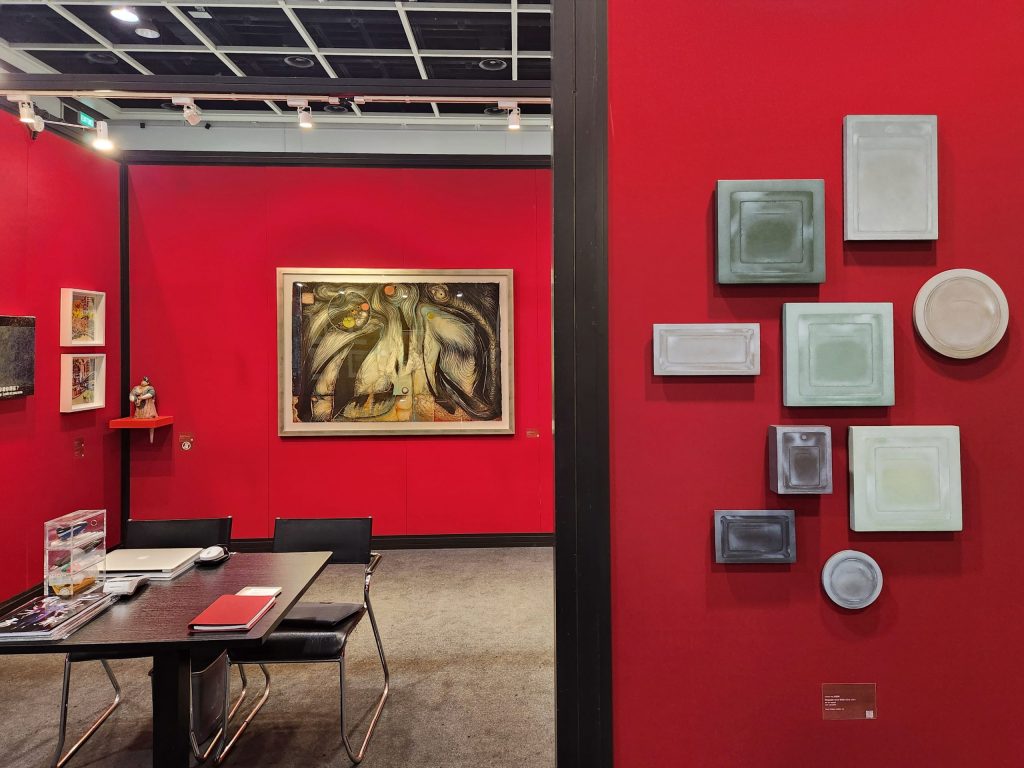 Interior view of Karin Weber Gallery's booth at Fine Art Asia 2023, Hong Kong, showing artworks displayed against deep red walls with a meeting table and seating area in the foreground.