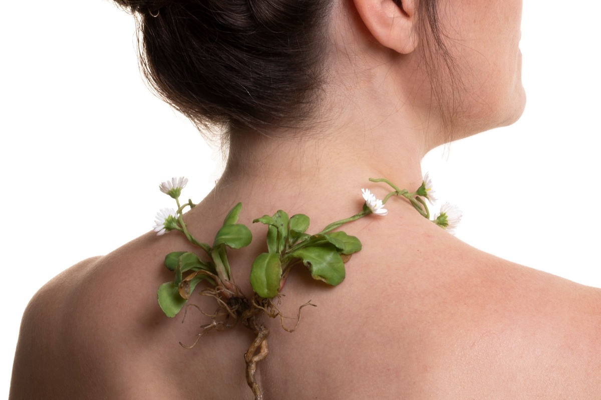 The artist wearing a wax daisy chain necklace with roots resting against a scar on her back.