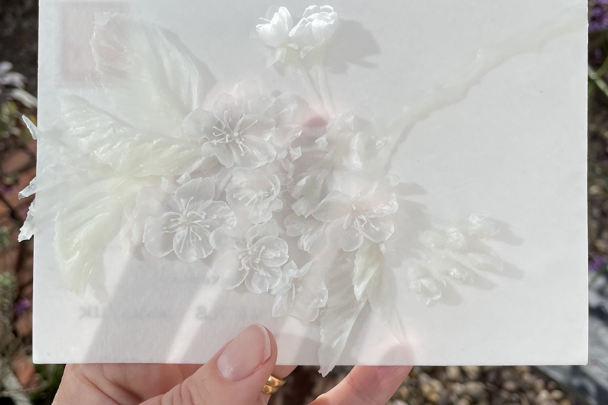 The artist holding a white wax-coated postcard with attached sculpted flowers.